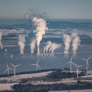 A giant smoking coal-fired power plant near the Czech-Polish border. In the foreground wind turbines producing greener energy.