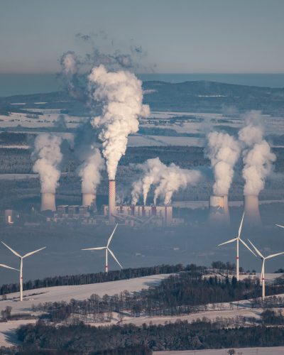A giant smoking coal-fired power plant near the Czech-Polish border. In the foreground wind turbines producing greener energy.