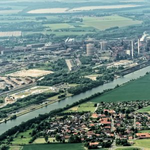 Salzgitter, Lower Saxony, Germany, May 24, 2018: Steelworks on the canal (Salzgitter-Stichkanal) between meadows and fields and a village in the foreground, heavy industry